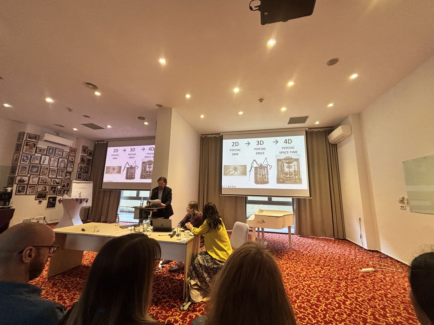 Jay Barlow prezintă la pupitru; pe două ecrane se vede slide-ul cu dimensiunile 2D, 3D și 4D